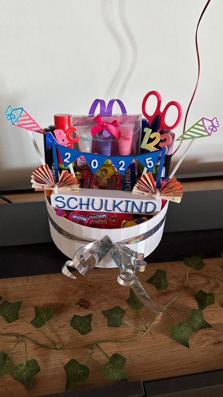 Einschulgeschenk Bunte Bastelutensilien und Dekoration in einem weißen Behälter auf einem Tisch.
